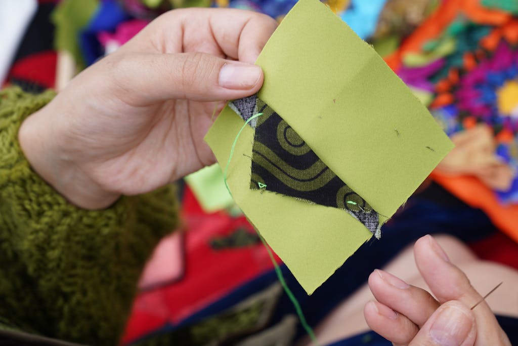 Close-up image of hands quilting with vibrant fabrics and intricate patterns, showcasing traditional sewing techniques.