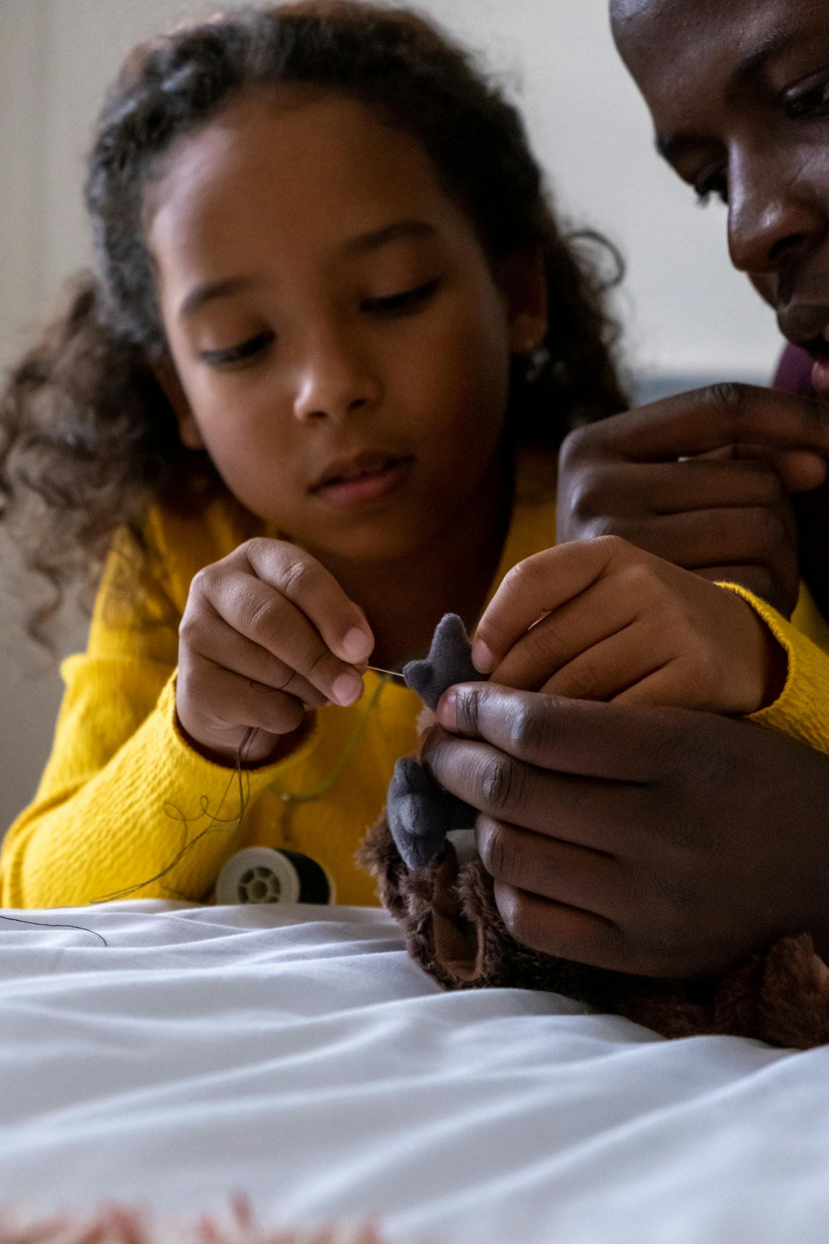 A father and daughter bonding over sewing indoors, focused on the needle and thread.